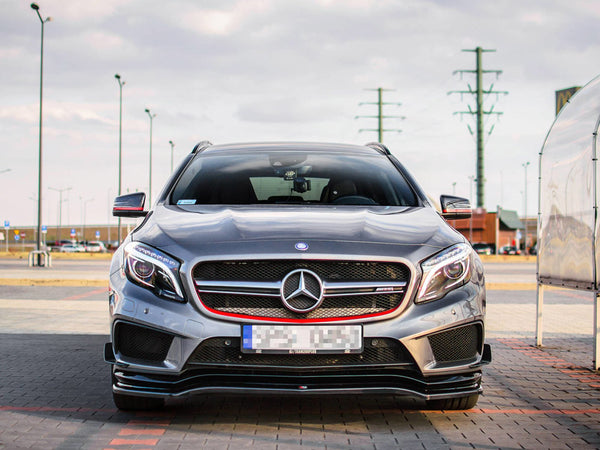 A silver Mercedes-Benz car is parked on a paved area. The setting is an open parking lot with utility poles and a cloudy sky in the background.