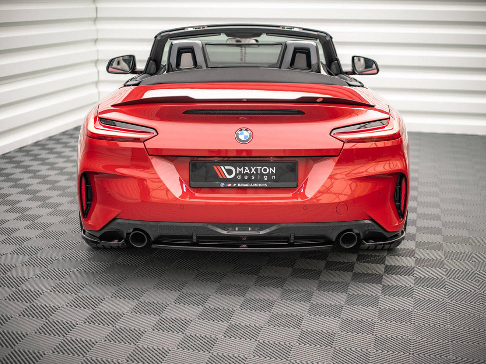 A red convertible sports car, viewed from the rear, sits on a textured floor in a white, ridged enclosure. The license plate reads "MAXTON design."