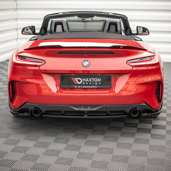 A red convertible sports car, viewed from the rear, sits on a textured floor in a white, ridged enclosure. The license plate reads "MAXTON design."