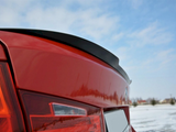 Red car trunk with a small spoiler. The car is stationary on a snow-covered field. The sky is clear with scattered clouds.