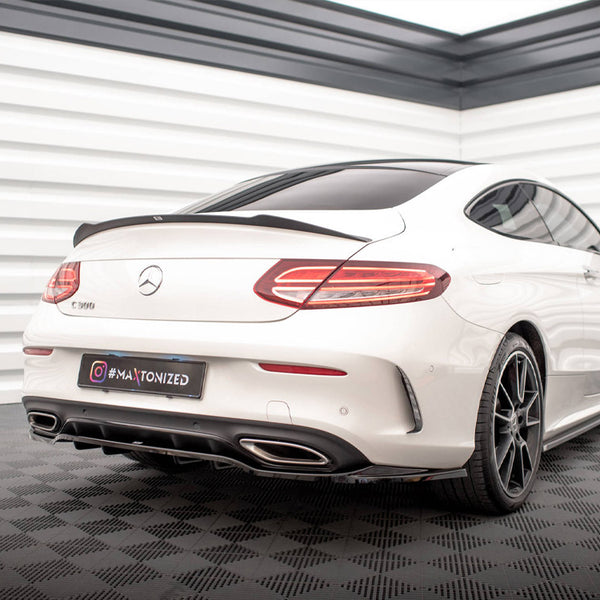 A white Mercedes-Benz C-Class coupe is stationary, displayed in a well-lit showroom with checkered flooring. The license plate reads "#MAXTONIZED."