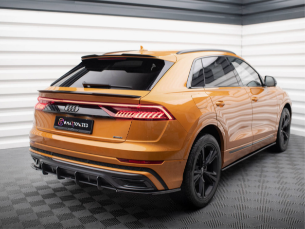 An orange Audi SUV is parked in a brightly lit room with patterned flooring and striped walls. The license plate reads "@IAMTONIZED."