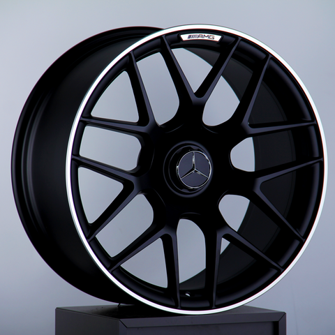 A black alloy wheel with a Mercedes-Benz logo and AMG branding is displayed upright on a dark pedestal against a plain gray background.