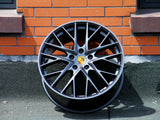 A car wheel rim with multiple spokes, displaying the Porsche logo, leans against an orange brick wall on a rough, paved surface.
