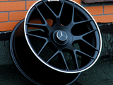 A black Mercedes-Benz AMG wheel rim leans against an orange brick wall on a dark concrete surface. The central emblem features the Mercedes logo.