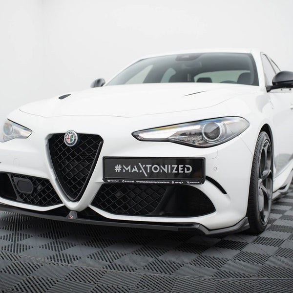 A white sports car is parked on a dark checkered floor in a studio setting. The car's front features a prominent grille, sleek headlights, and a license plate reading "#MAXTONIZED."
