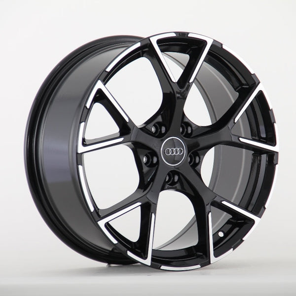 A black and silver Audi wheel rim with a five-spoke design is displayed against a plain white background. The Audi logo is centered on the wheel hub.