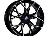 A black and silver alloy wheel with a geometric design features the BMW logo in the center, positioned against a plain white background.