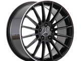A black, multi-spoke alloy wheel stands upright, featuring a prominent silver Mercedes-Benz emblem in the center. It is set against a plain white background, emphasizing its sleek design.