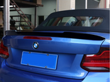A blue convertible car with the top down is parked in a garage with tiled walls and a staircase. The back features a BMW logo and blurred license plate.