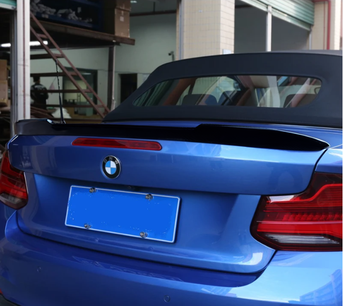 A blue convertible car with the top down is parked in a garage with tiled walls and a staircase. The back features a BMW logo and blurred license plate.