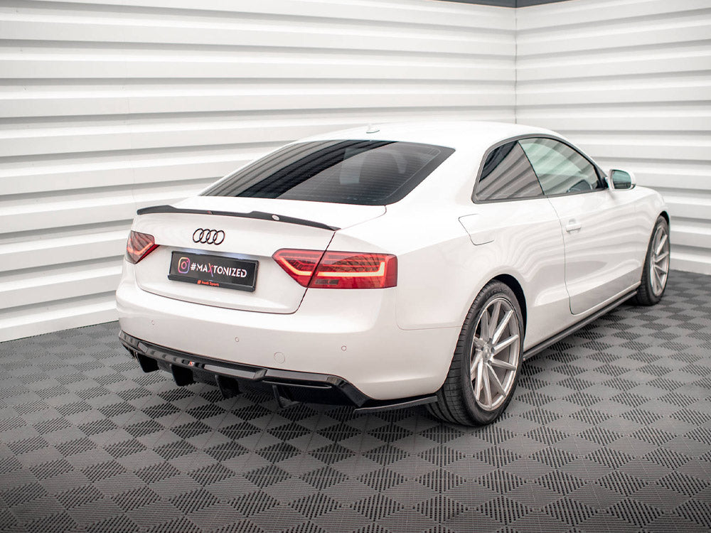 A white Audi coupe parked in a showroom with textured flooring and corrugated walls. The license plate reads “#MAXTONIZED.”