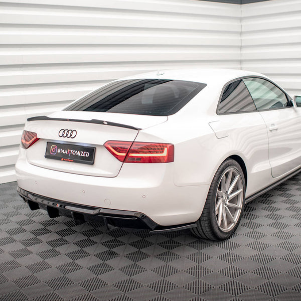 A white Audi coupe parked in a showroom with textured flooring and corrugated walls. The license plate reads “#MAXTONIZED.”
