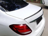 A white car is parked with visible red taillights. It has a black spoiler on the trunk. Nearby, other vehicles and trees are visible.