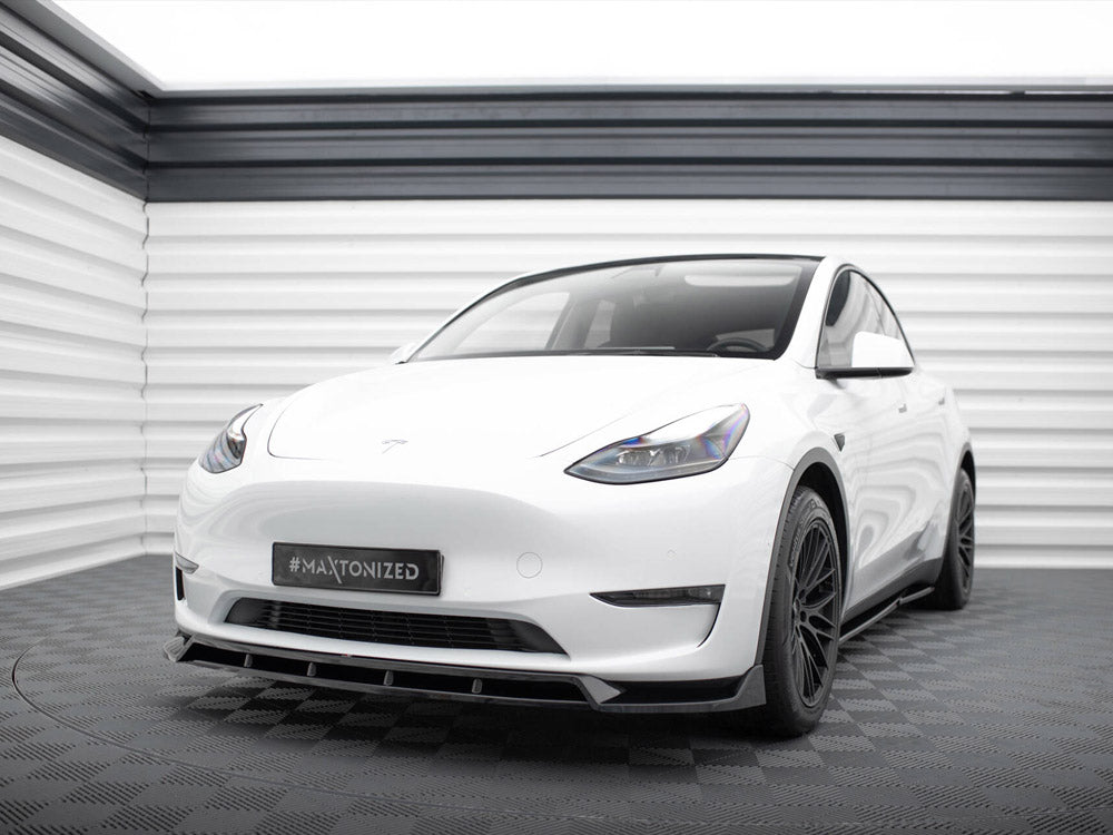 A white car stands on a checkered floor within a sleek, modern garage. The license plate reads "#MAXTONIZED."