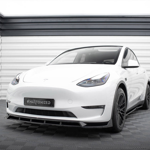 A white car stands on a checkered floor within a sleek, modern garage. The license plate reads "#MAXTONIZED."