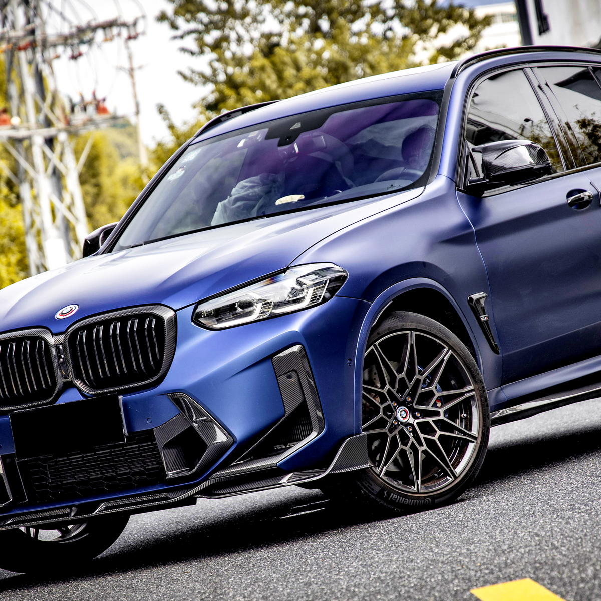 A blue SUV is parked on a street with trees and utility poles in the background. The car features sleek design elements and dark alloy wheels, indicating a sporty appearance.