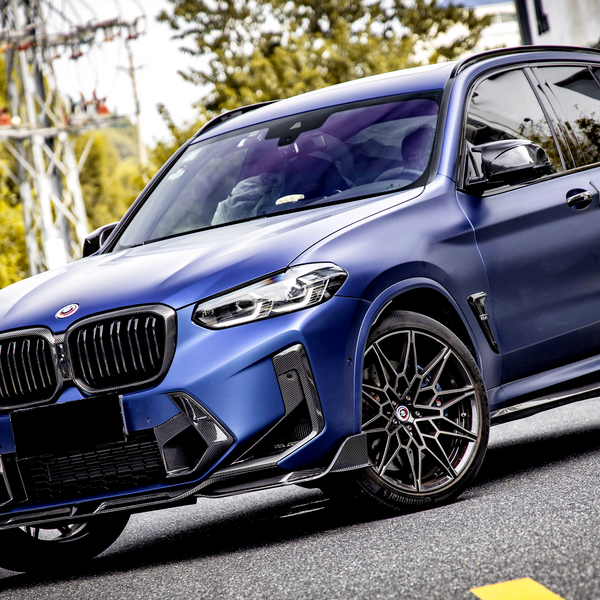 A blue SUV is parked on a street with trees and utility poles in the background. The car features sleek design elements and dark alloy wheels, indicating a sporty appearance.