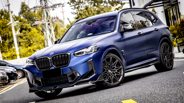 A blue SUV is parked on a street with trees and utility poles in the background. The car features sleek design elements and dark alloy wheels, indicating a sporty appearance.