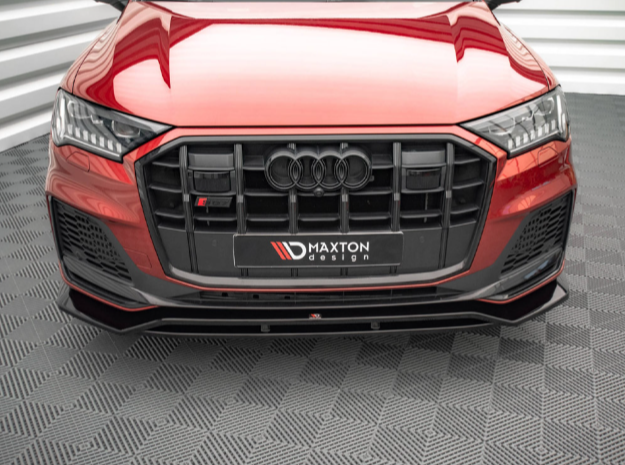 A red Audi with a black front grille is stationary on a patterned floor. "Maxton Design" is written on the license plate frame. The environment is indoors with white walls.