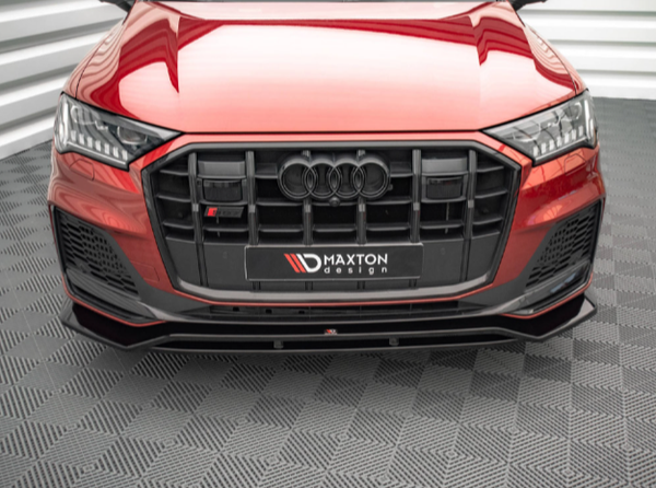 A red Audi with a black front grille is stationary on a patterned floor. "Maxton Design" is written on the license plate frame. The environment is indoors with white walls.