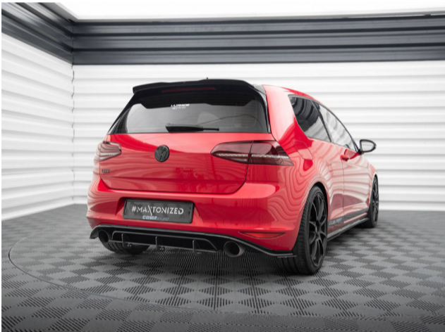 A red car is parked, displayed in a modern showroom with patterned flooring and striped walls. Text on the car's rear window reads "Maxton Design," and the plate reads "#MAXTONIZED."