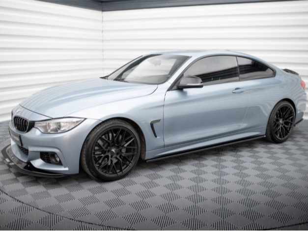 A sleek silver coupe with black wheels is parked in a modern, white garage featuring a patterned gray floor, highlighted by reflective surfaces and soft lighting.