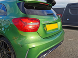 Green Mercedes A 200 d car parked with a spoiler and tinted windows visible, surrounded by a gray vehicle on an asphalt surface. License plate is obscured.