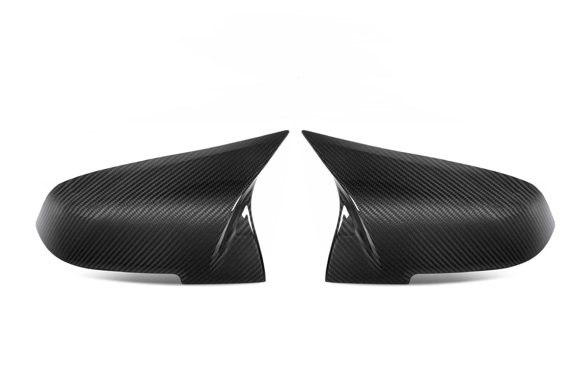 Two carbon fiber side mirror covers face each other on a white background, displaying a sleek, aerodynamic design with subtle texture and reflective finish. No text present.