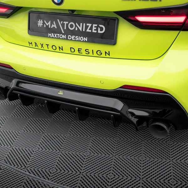 A bright yellow car with a black diffuser and dual exhausts is parked on a patterned surface. Visible text: "#MAXTONIZED, MAXTON DESIGN," printed on a license plate and bumper.