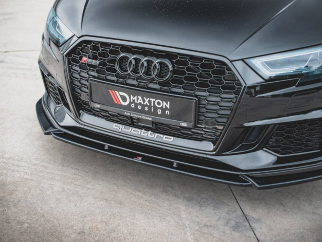 A black car's front grille displays its brand logo with a sleek design. The license plate reads "MAXTON design," and "quattro" is on the lower bumper. The car is parked on concrete.