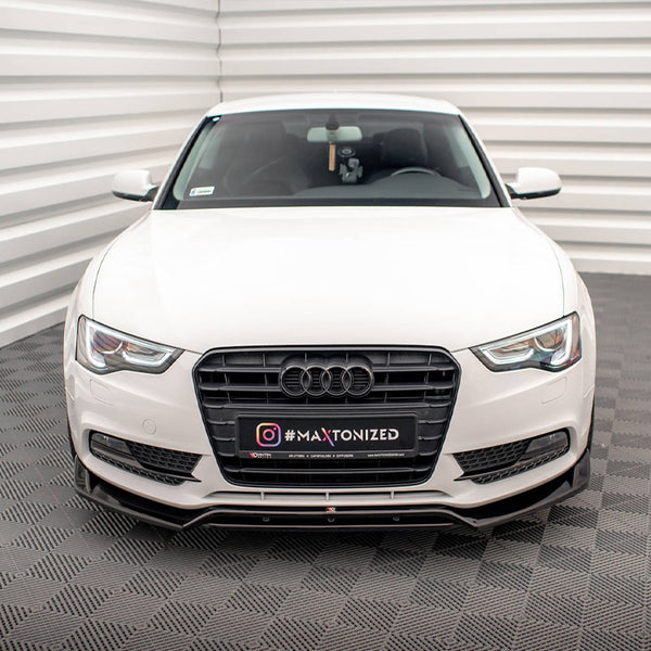 A white Audi car is parked in a patterned indoor space with textured floors and walls. The front license plate displays "#MAXTONIZED."
