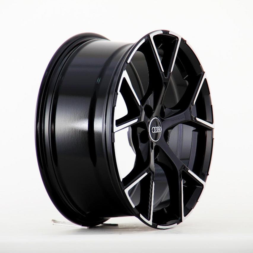 A sleek black alloy wheel with a multi-spoke design rests upright against a plain white background. The center features the Audi logo, providing a polished and modern look.