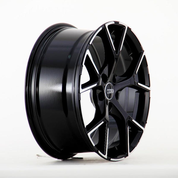 A sleek black alloy wheel with a multi-spoke design rests upright against a plain white background. The center features the Audi logo, providing a polished and modern look.