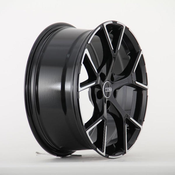 A black alloy wheel with a sleek, silver-accented design is standing upright against a plain white background. The center features a logo with four interlocking rings.