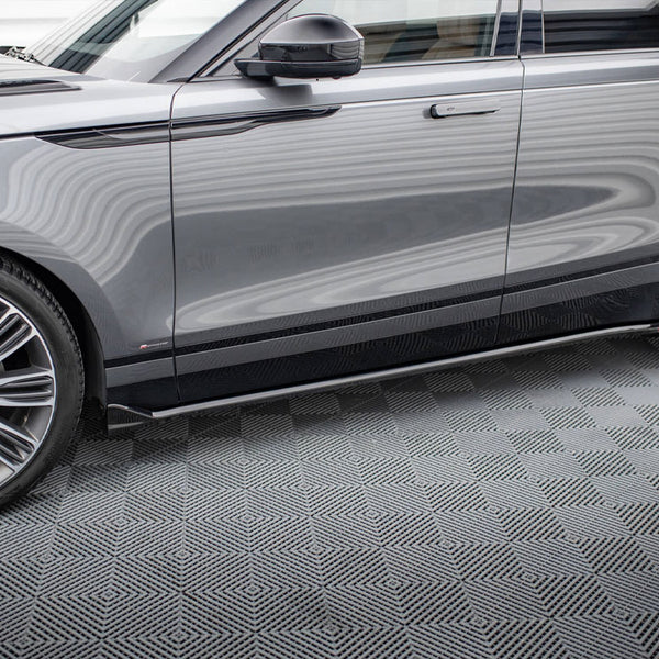 A gray SUV is parked indoors on a patterned floor. The vehicle's shiny surface reflects wavy lines, a black handle is visible, and large chrome wheels dominate the foreground.