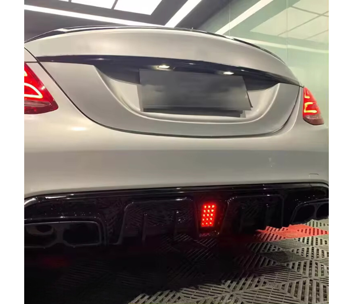 A white car's rear features illuminated taillights and a glowing red light on the diffuser. It's parked indoors on a patterned floor, with soft overhead lighting.
