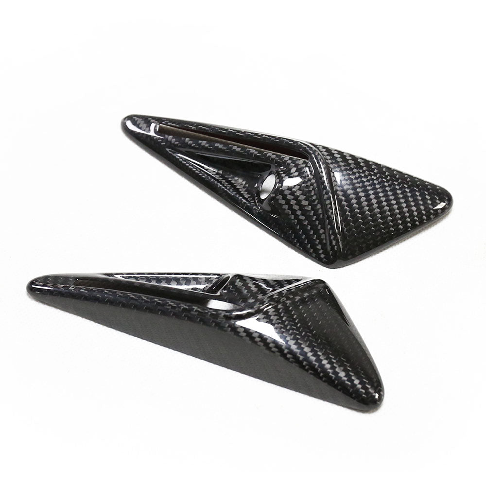 Two carbon fiber aerodynamic winglets, featuring a glossy finish, lie on a plain white surface. The winglets have a sleek, triangular shape with textured patterning.