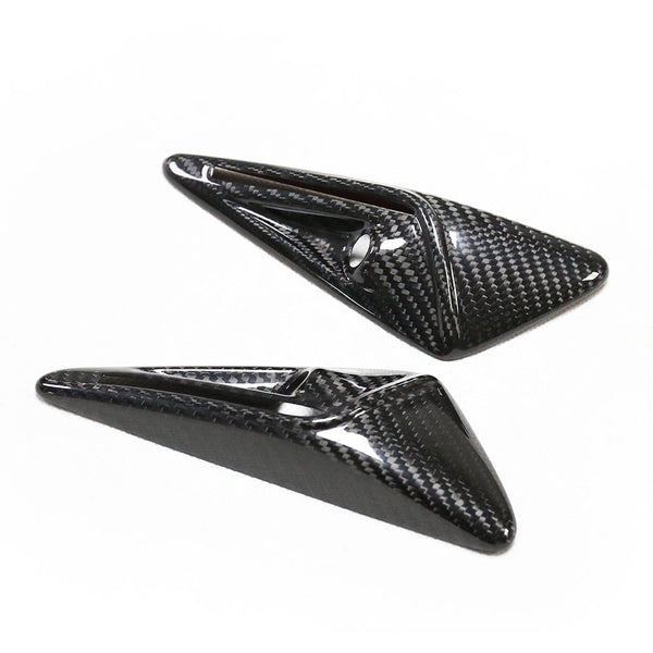 Two carbon fiber aerodynamic winglets, featuring a glossy finish, lie on a plain white surface. The winglets have a sleek, triangular shape with textured patterning.