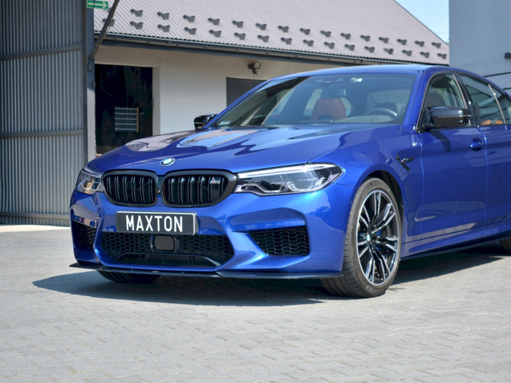 A blue BMW car is parked on a cobblestone surface beside a modern building. The license plate reads "MAXTON."