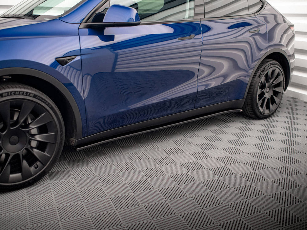 A blue car with black wheels parked in a room with a patterned gray floor and white corrugated walls. The tire reads "MICHELIN."