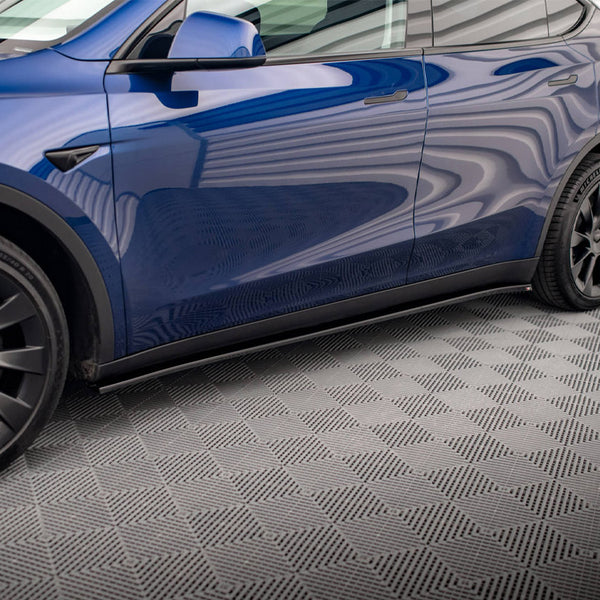 A blue car with black wheels parked in a room with a patterned gray floor and white corrugated walls. The tire reads "MICHELIN."
