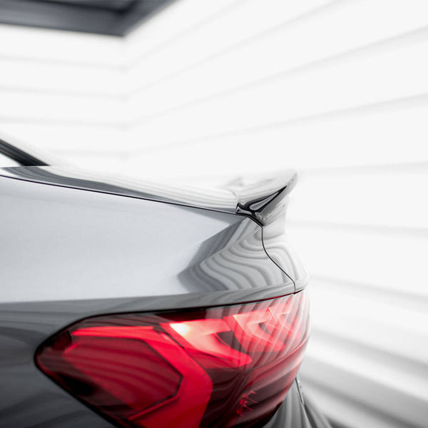 A sleek car's rear with a dark metallic finish and tail light glowing red, parked in a bright, modern, white-paneled environment.