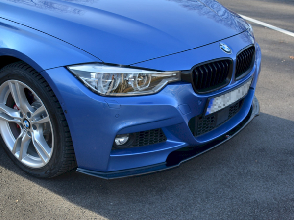 A blue car is parked on a paved surface, displaying its front section with a prominent grille, headlight, and wheel. No visible text is present.