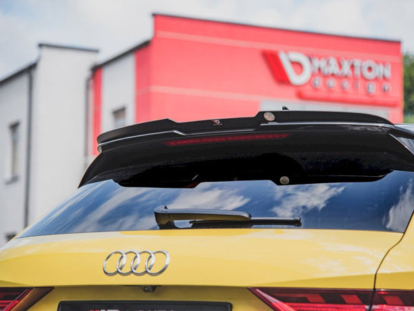 Yellow Audi parked with rear view featuring a spoiler and license plate. Behind, a red building displays the text "MAXTON design." The sky is partly cloudy.