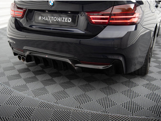 A sleek black car's rear end with illuminated taillights is parked on a patterned floor. The license plate reads "#MAXTONIZED."