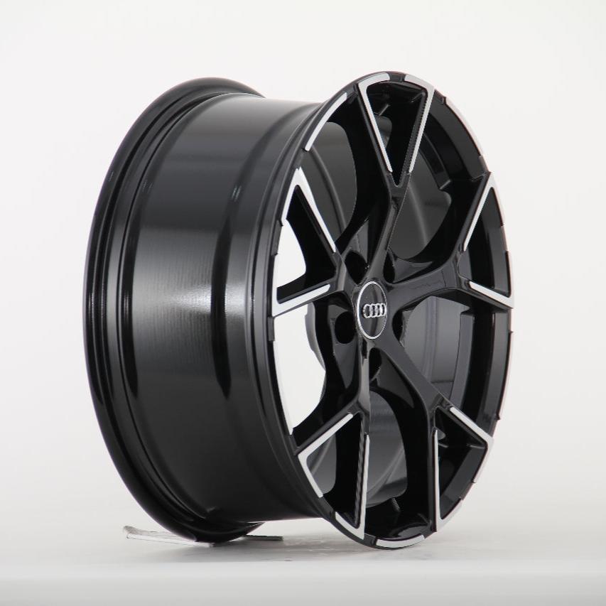 A glossy black alloy wheel with a multi-spoke design featuring a central Audi logo, stands on display against a plain white background.