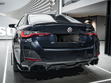 A sleek, dark-colored car is parked in a showroom with a modern design. The car's rear features prominent taillights and quad exhaust pipes. The wall has text: 