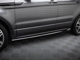 A grey SUV side, with polished metallic running boards, is parked on a patterned floor. The vehicle has clean lines and sleek wheel rims, indicating a modern design.