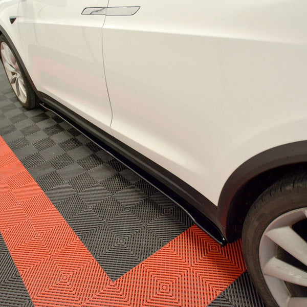 A white car is parked, showcasing its side and wheel, on a black and red checkered garage floor, providing a visually striking contrast.